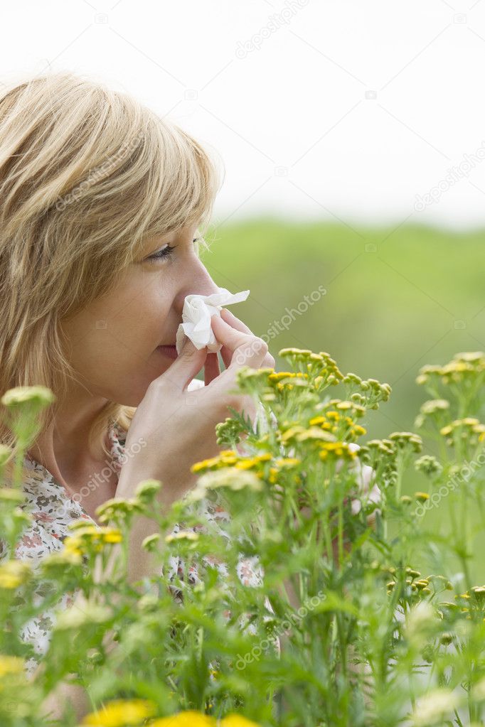 Woman blowing nose into tissue outdoors