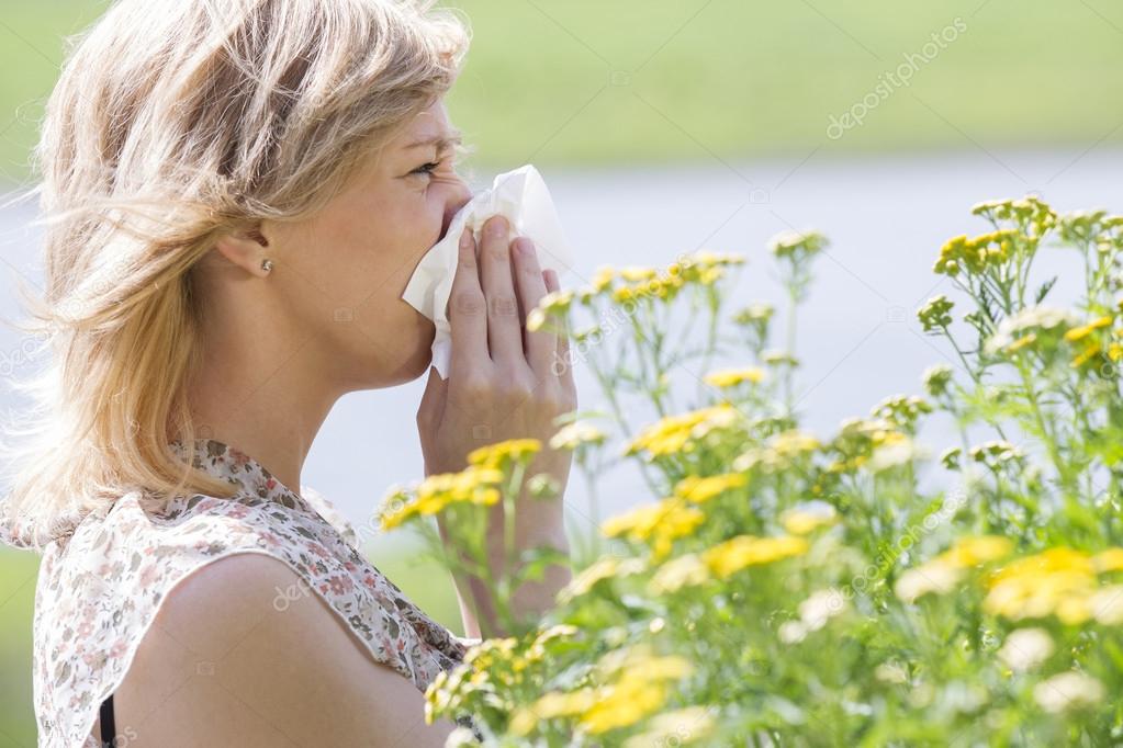 Woman blowing nose into tissue in front of flowers