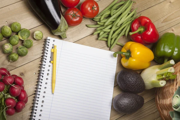 Vegetables with book and pen on wooden surface — Stock Photo, Image