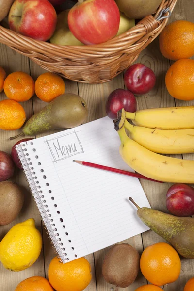 Various fruits in basket with pencil and book — Stock Photo, Image