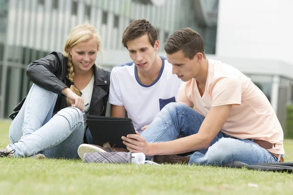 Drie studenten kijken naar een ipad — Stockfoto