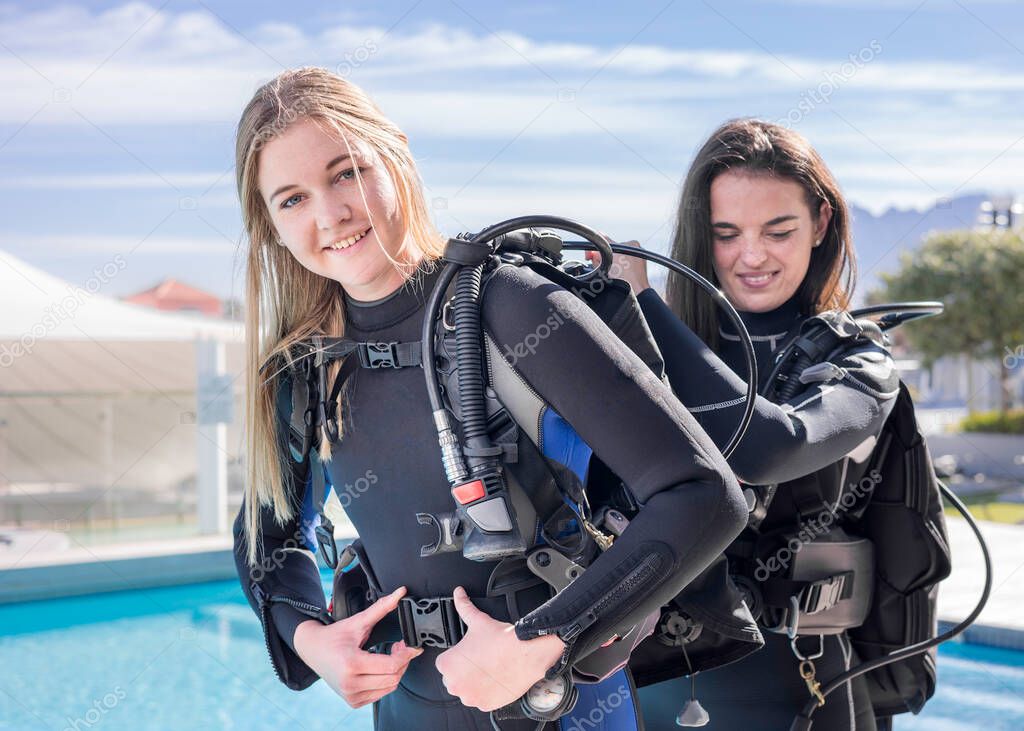 Scuba divers helping each other to put their gear on next to a pool
