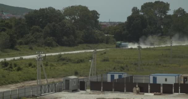 Een vrachtwagen rijdt langs een stoffige weg langs een bouwplaats — Stockvideo