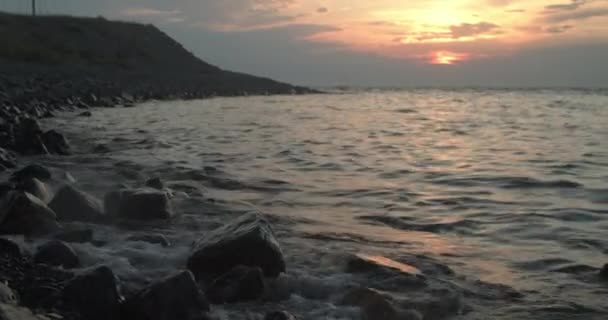 Ευρεία παραλία γωνία στο ηλιοβασίλεμα με τον ήλιο αντανακλάται στον ωκεανό και τα κύματα πιτσιλίζουν πάνω σε βράχους — Αρχείο Βίντεο