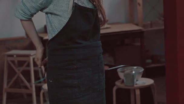 Une fille en atelier de poterie met un tablier. Fabrication de produits en céramique à partir d'argile blanche . — Video