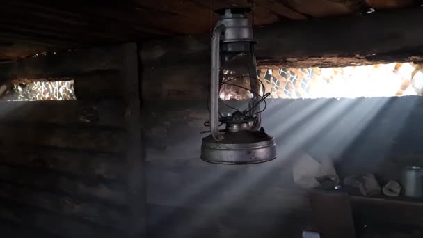 Drewniana ławka, w której pali się lampa naftowa. Światło z okna przenika do pokoju.. — Wideo stockowe