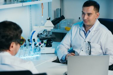 Tıbbi Geliştirme Laboratuvarı: Mikroskop altında Yüz Maskesi Giyen Bilim adamı.