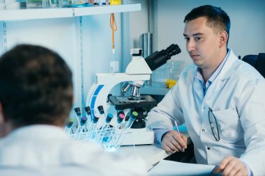 Tıbbi Geliştirme Laboratuvarı: Mikroskop altında Yüz Maskesi Giyen Bilim adamı.