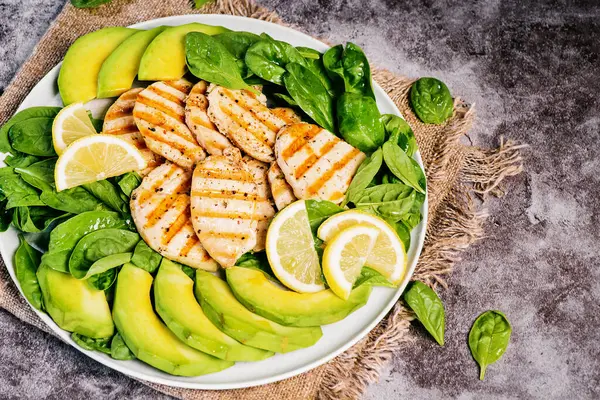 Grilled chicken fillet with avocado slices and spinach. Healthy food. Diet food.Light grilled chicken breast salad with avocado slices. Light gray background. view from above. High quality photo