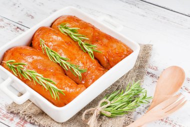 Taze biberiye yaprakları ve baharatlarla birlikte beyaz bir tabakta kırmızı soslu çiğ tavuk filetosu. Taze marine edilmiş tavuk eti..