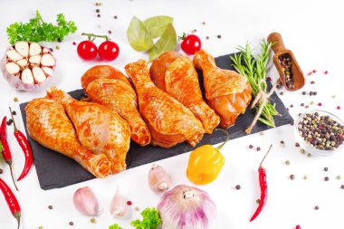 Barbekü soslu tavuk dramsticks siyah mutfak tahtası, taze biberiye yapraklı beyaz arka plan ve kiraz domatesleri, çeşitli baharatlar, yakın plan. Yarı bitmiş ürün, çabuk pişirme..