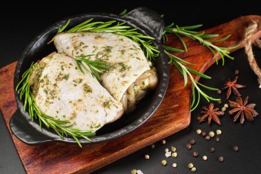 Çiğ et tavuğu. Çiğ tavuk budu. Bitki sosuyla marine edilmiş. Arka planda taze biberiye ve baharatlar var. Baharatlı tavuk budu, sarımsak.