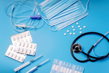 Tıbbi steteskoplu, şırıngalı, haplı üst düzey doktor masası. Sağlık ve tıp konsepti. Steteskop, makas, şırınga ve kapsüller de dahil olmak üzere tıbbi ekipmanlar mavi arka planda..