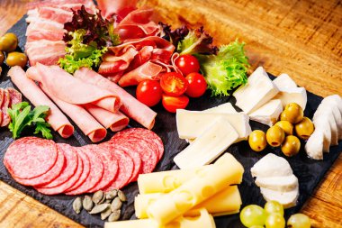 Şarküteri, salam, peynir, camembert ve zeytin içeren antipasti tabağı. Ahşap masa üzerinde çeşitli et ve sosisler. Peynirli Antipasto tabağı..