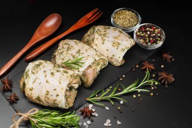 Hafif soslu çiğ tavuk budu, otlar ve baharatlarla birlikte koyu bir arka planda otlar. Yarı pişmiş tavuk butları. Manzaralı. Çiğ tavuk marine edildi..