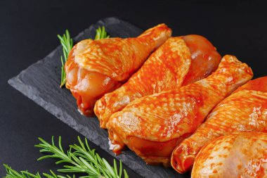 Siyah arka planda siyah bir yemek tahtasında taze biberiye yapraklarıyla marine edilmiş ızgara tavuk dolması. Yarı bitmiş ürün, marine edilmiş ürün, hızlı pişirme..