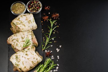 Hafif soslu çiğ tavuk budu, otlar ve baharatlarla birlikte koyu bir arka planda otlar. Yarı pişmiş tavuk butları. Manzaralı. Çiğ tavuk terbiye edildi. Anlaşıldı..