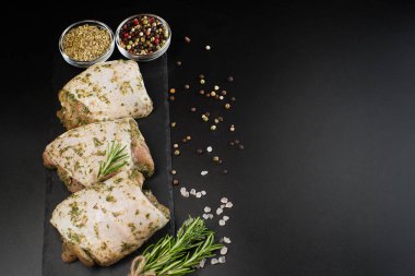 Çiğ et tavuğu. Çiğ tavuk budu. Bitki sosuyla marine edilmiş. Arka planda taze biberiye ve baharatlar var. Baharatlı tavuk budu, sarımsak. Boşluğu kopyala..