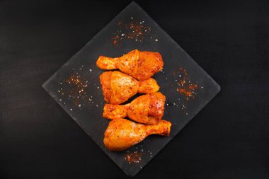 Çiğ tavuk bacağı. Lezzetli marine edilmiş tavuk bacağı. Harika görünüyor. Siyah arka planda biberiye serpiştirilmiş ızgara tavuk bacağı..