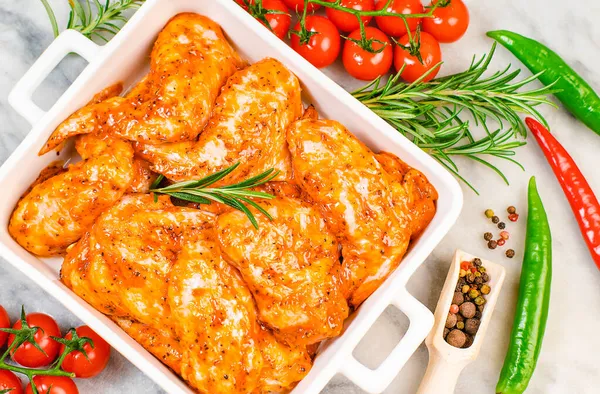 Marinated chicken wings in red sauce in a white ceramic plate for oven baking with vegetables. Oven baking wings. Semifinished. Fast cooking.Raw Marinated chicken meat wings for BBQ,