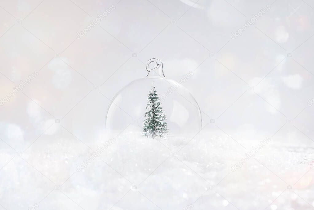 Greeting card, banner, poster.Soft focus.Shiny, glass Christmas ball with a miniature Christmas tree on the snow on a light background.Christmas composition.Shiny background.copy space.