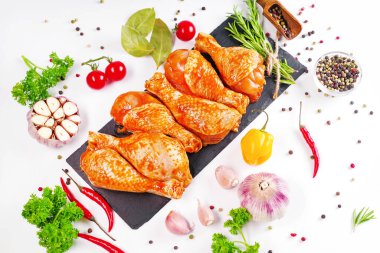 Barbekü soslu tavuk dramsticks siyah mutfak tahtası, taze biberiye yapraklı beyaz arka plan ve kiraz domatesleri, çeşitli baharatlar, yakın plan. Yarı bitmiş ürün, çabuk pişirme..