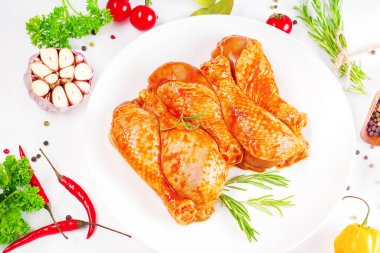 Barbekü soslu tavuk dramsticks siyah mutfak tahtası, taze biberiye yapraklı beyaz arka plan ve kiraz domatesleri, çeşitli baharatlar, yakın plan. Yarı bitmiş ürün, çabuk pişirme..