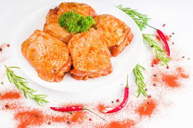 Çiğ tavuk butları kırmızı sosla marine edilmiş beyaz tabakta, beyaz tabakta taze biberiye ve kırmızı acı biberle. Tavuk yarı pişmiş kalçalar..