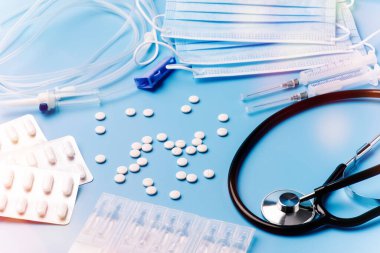 Tıbbi steteskoplu, şırıngalı, haplı üst düzey doktor masası. Sağlık ve tıp konsepti. Steteskop, makas, şırınga ve kapsüller de dahil olmak üzere tıbbi ekipmanlar mavi arka planda..