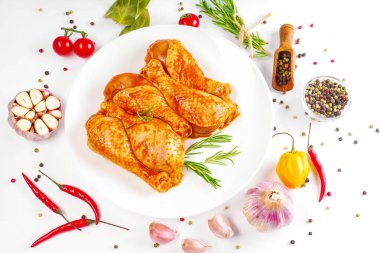 Barbekü soslu tavuk dramsticks siyah mutfak tahtası, taze biberiye yapraklı beyaz arka plan ve kiraz domatesleri, çeşitli baharatlar, yakın plan. Yarı bitmiş ürün, çabuk pişirme..