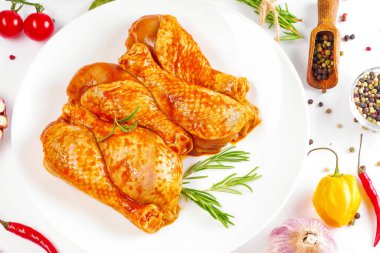 Barbekü soslu tavuk dramsticks siyah mutfak tahtası, taze biberiye yapraklı beyaz arka plan ve kiraz domatesleri, çeşitli baharatlar, yakın plan. Yarı bitmiş ürün, çabuk pişirme..