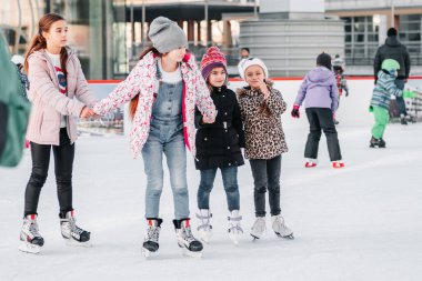 Yumuşak, seçici odaklanma. İnsanlar, arkadaşlık, spor ve eğlence kavramı - mutlu arkadaşlar buz pistinde kayıyor. Bir grup genç arkadaş buz pateni yaparken dinleniyor..