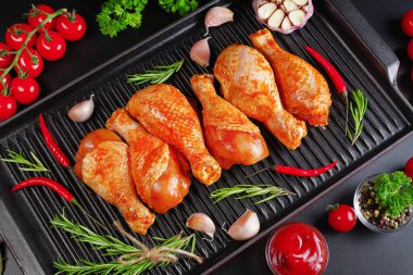 Kırmızı sosla marine edilmiş çiğ tavuk bacağı koyu bir arka planda, kırmızı acı biberli domates ve sarımsaklı ızgara tavada. Tavuk yarı pişmiş bacakları. Manzaralı. Çiğ tavuk marine edildi..