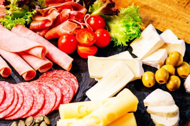 Şarküteri, salam, peynir, camembert ve zeytin içeren antipasti tabağı. Ahşap masa üzerinde çeşitli et ve sosisler. Peynirli Antipasto tabağı..
