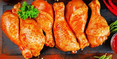 Baharatlı arka plan afişi. Barbekü marine edilmiş tavuk çubukları siyah bir arkaplanda taze biberiye yapraklarıyla birlikte siyah bir yemek tahtasında. Yarı bitmiş ürün, marine edilmiş ürün, pişirme..