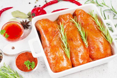 Terbiye edilmiş taze tavuk eti. Kırmızı soslu çiğ tavuk filetosu. Beyaz bir tabakta taze biberiye yaprakları ve baharatlarla birlikte..