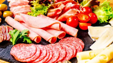 Lezzetli İspanyol sosis salamı dilimleri. Sağlıklı gıda kavramı. Salamlı jambon, sosis, zeytin ve baharat çeşitleri. Siyah masada farklı domatesli farklı türde sosisler..