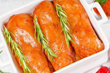 Çiğ salamura edilmiş tavuk filetosu ve taze biberiye. Hafif bir arka planda fırında kızarmak için kırmızı soslu marine edilmiş tavuk filetosu..