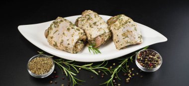 Bitkisel sosla marine edilmiş çiğ tavuk butları. Arka planda taze biberiye ve baharatlar var. Baharatlı tavuk budu, sarımsak.