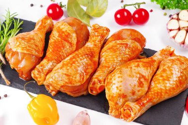 Barbekü soslu tavuk dramsticks siyah mutfak tahtası, taze biberiye yapraklı beyaz arka plan ve kiraz domatesleri, çeşitli baharatlar, yakın plan. Yarı bitmiş ürün, çabuk pişirme..
