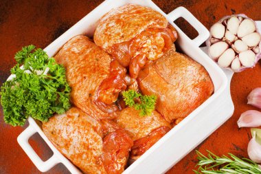 Kırmızı sosla marine edilmiş tavuk butları bir kabın içinde otlar ve sarımsakla. Terbiye edilmiş tavuk parçaları. Yarı bitmiş ürün, hızlı pişirme..