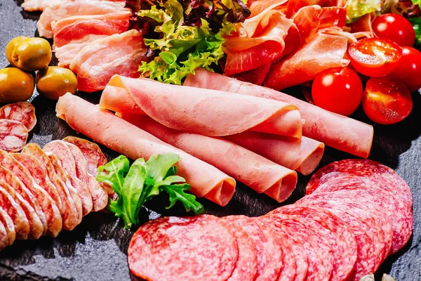 Siyah masa üzerinde farklı türde domatesli sosisler servis edilir. Salam jambon, sosis, zeytin ve baharat çeşitleri. Et aperatifi. Güzel manzara. Sağlıklı gıda konsepti..