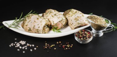 Bitkisel sosla marine edilmiş çiğ tavuk butları. Arka planda taze biberiye ve baharatlar var. Baharatlı tavuk budu, sarımsak.