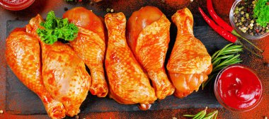 Baharatlı arka plan afişi. Barbekü marine edilmiş tavuk çubukları siyah bir arkaplanda taze biberiye yapraklarıyla birlikte siyah bir yemek tahtasında. Yarı bitmiş ürün, marine edilmiş ürün, pişirme..