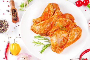 Barbekü soslu tavuk dramsticks siyah mutfak tahtası, taze biberiye yapraklı beyaz arka plan ve kiraz domatesleri, çeşitli baharatlar, yakın plan. Yarı bitmiş ürün, çabuk pişirme..