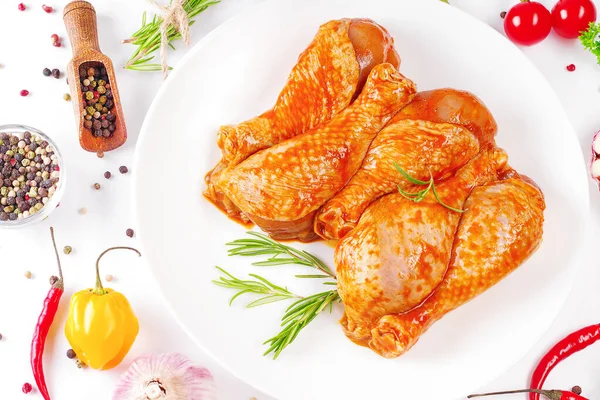 Barbekü soslu tavuk dramsticks siyah mutfak tahtası, taze biberiye yapraklı beyaz arka plan ve kiraz domatesleri, çeşitli baharatlar, yakın plan. Yarı bitmiş ürün, çabuk pişirme..