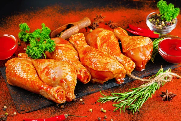 Barbeque marinated chicken dramsticks on a black cooking board on a black background with fresh rosemary leaves. Semi-finished product, Marinated product,cooking.Background banner of meat with spices.