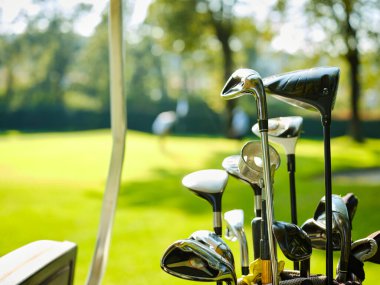 Golf çantası ve golf sopaları güneşli bir yaz gününde golf sahasının kenarında bir golf arabasının içinde. Ön planda golf sopaları.