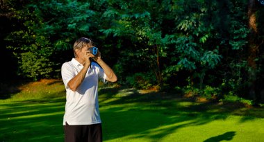 Golfçü, lazer mesafe buluculu bir golf sahasında bayrağa olan mesafeyi doğru bir şekilde ölçer. Arka planda orman var..