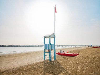 Cankurtaran kulesi, güneşli bir yaz sabahı sahilde bir cankurtaran botunun yanında arka planda İtalya 'nın Adriyatik kıyısında serinleyen banyocular var..
